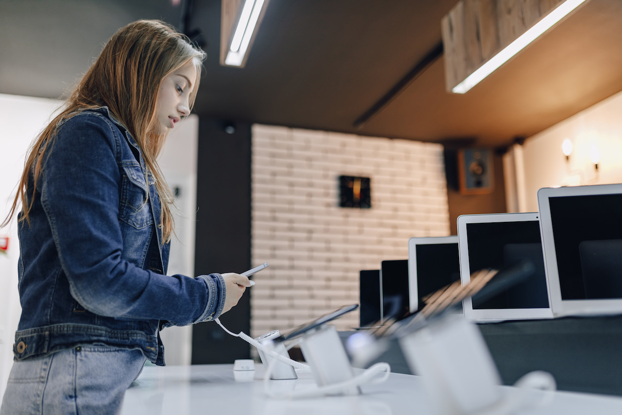 chica-la-industria-joven-atractiva-tienda-electronica-encuentra-escritorio-prueba-telefono